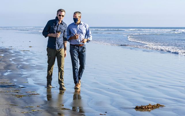 El gobernador de California, Gavin Newsom, a la izquierda, camina con Wade Crowfoot, Secretario de Recursos Naturales de California, a lo largo de State Beach en Huntington Beach, California, sitio del reciente derrame de petróleo en alta mar.