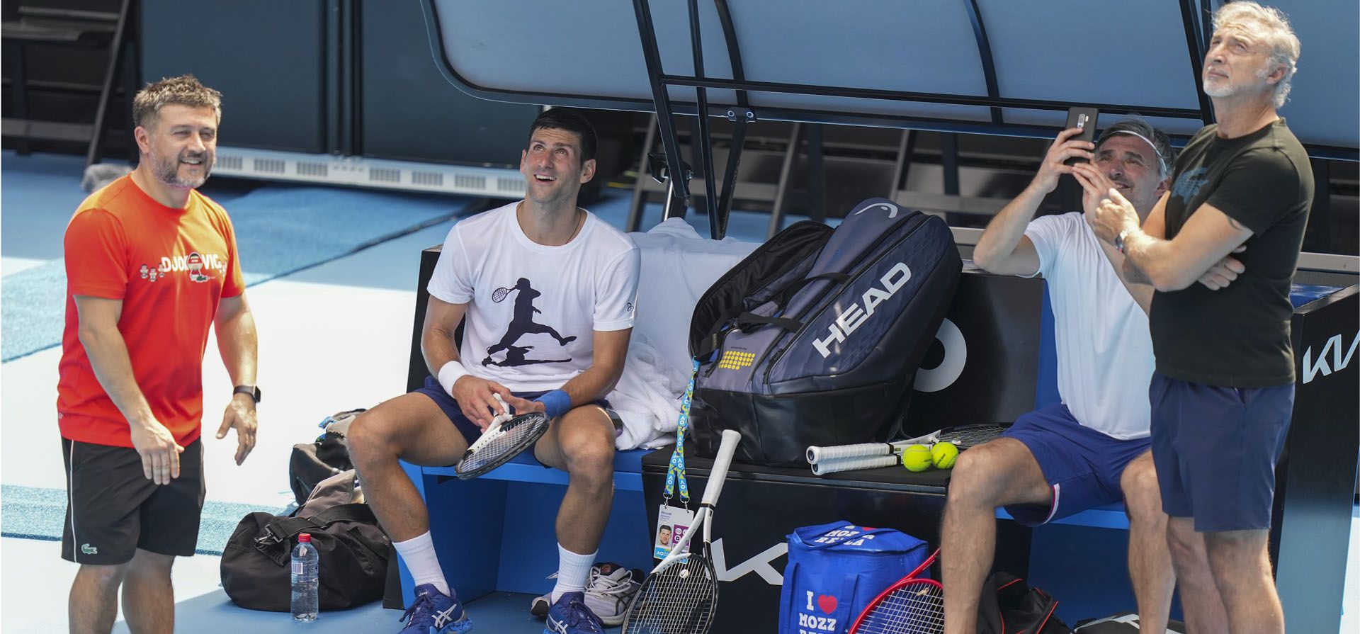 En esta foto proporcionada por Australia Open, el campeón defensor, Novak Djokovic, habla con un miembro de su equipo durante una sesión de práctica en el Rod Laver Arena en Melbourne Park en Melbourne, Australia. Los primeros ministros de Australia y Serbia discutieron la precaria visa de Novak Djokovic luego de que la estrella de tenis serbia mejor clasificada ganó una batalla judicial para competir en el Abierto de Australia, pero aún enfrenta la amenaza de deportación porque no está vacunado contra COVID- 19.