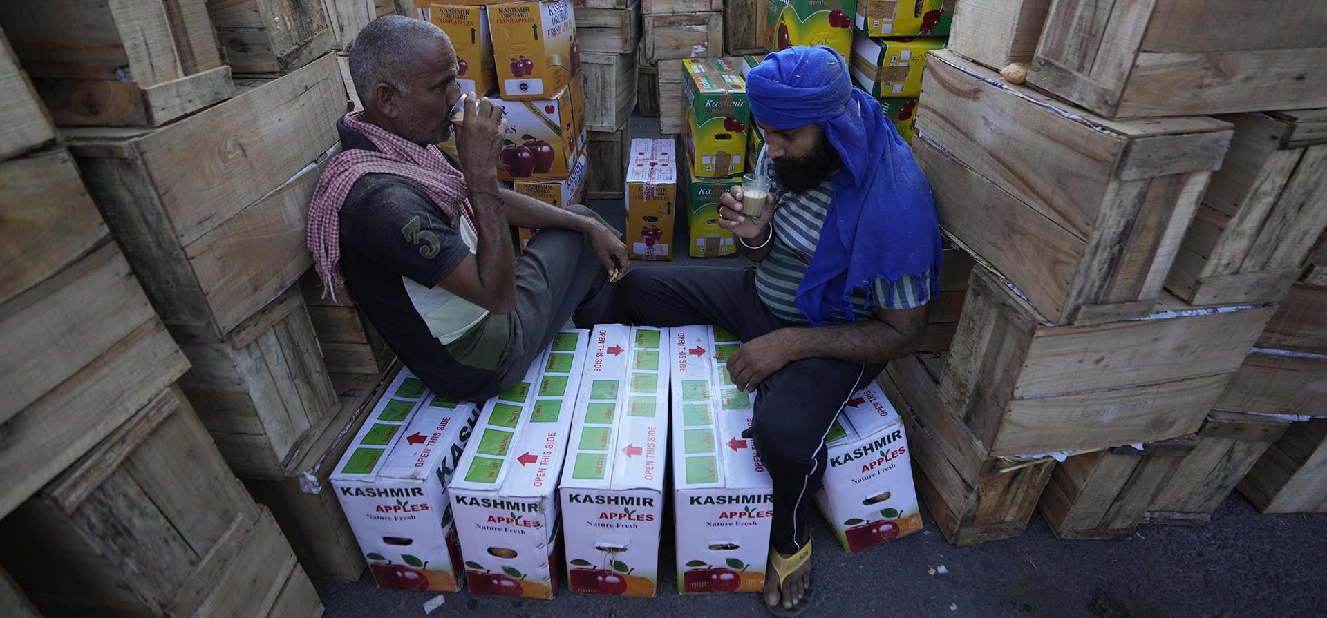 Trabajadores beben té sentados en cajas de manzanas en un mercado mayorista en Jammu, India, el miércoles 7 de septiembre de 2022. Jammu y Cachemira son los mayores productores de manzanas en la India.