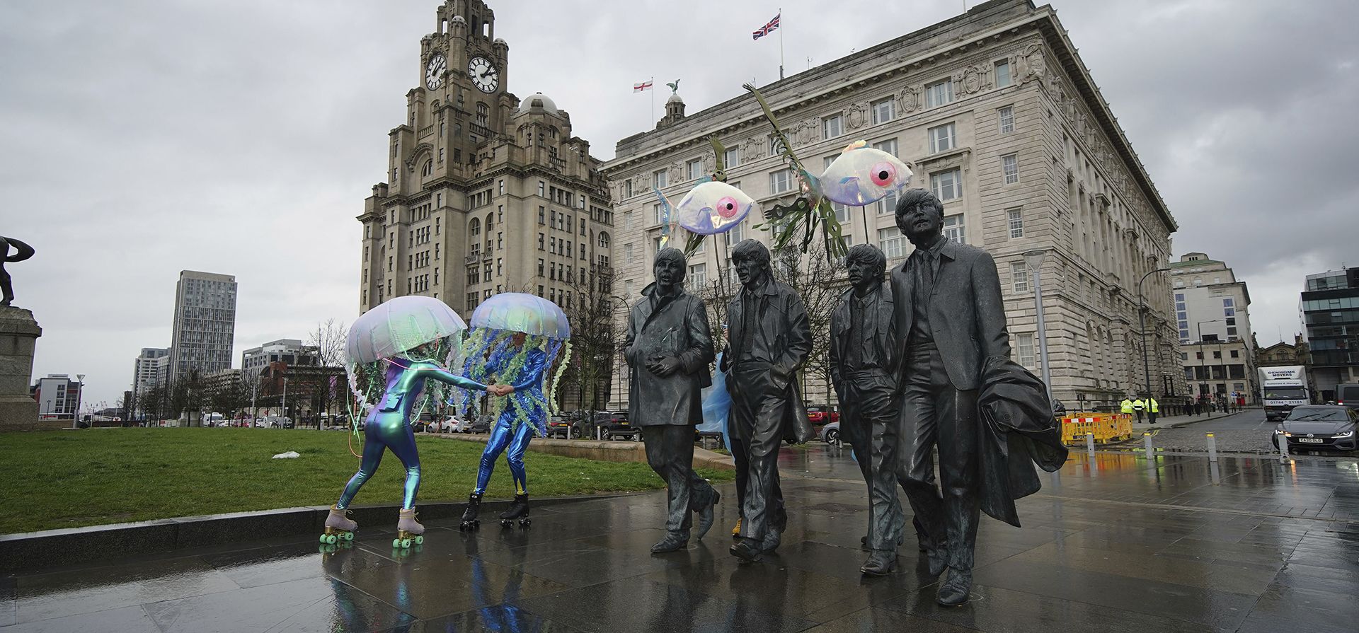 Artistas vestidos como medusas en patines patinan alrededor de la estatua de los Beatles en el lanzamiento del Eurovision EuroFestival en el British Music Experience en Liverpool, Inglaterra, el martes 28 de marzo de 2023. (Peter Byrne/PA vía AP)