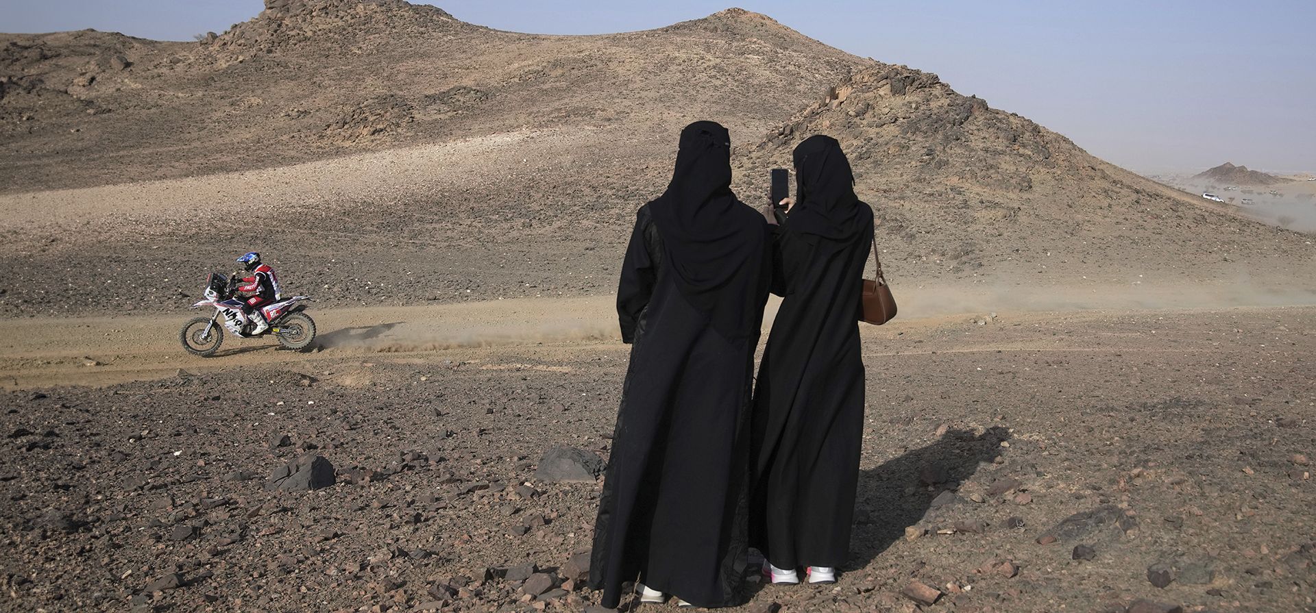 Unas mujeres toman fotografías del italiano Andrea Winkler mientras conduce durante el prólogo del Rally Dakar en Bisha, Arabia Saudita, el viernes 3 de enero de 2025. (Foto AP/Christophe Ena)