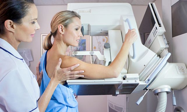 Nurse preparing patient for mammogram at x-ray machine in hospital