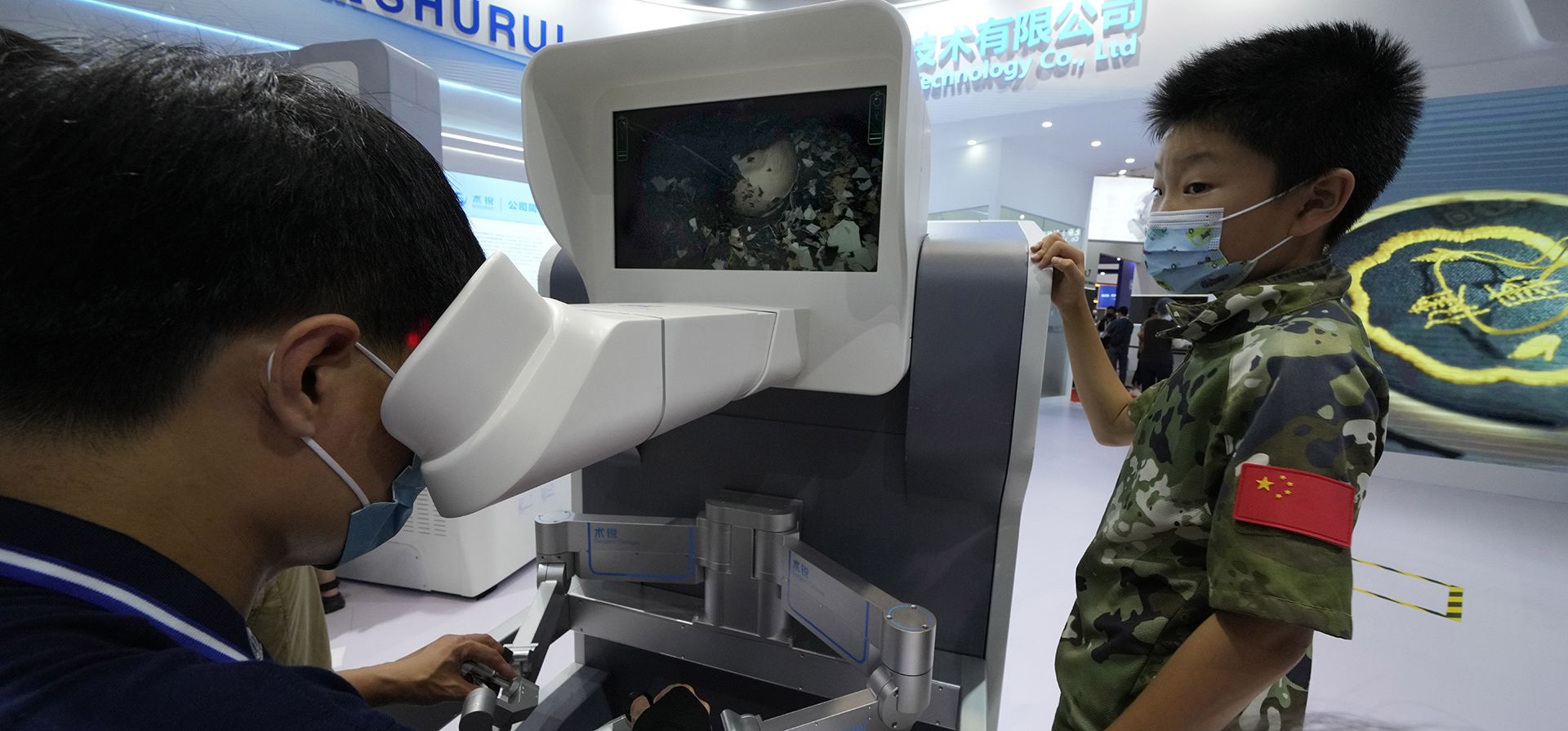 Un niño observa cómo un trabajador opera de forma remota un robot quirúrgico demostrando su destreza quitando la cáscara de un huevo durante la Conferencia Mundial de Robots en el Centro Internacional de Conferencias y Exposiciones de Yichuang en Beijing, el viernes 19 de agosto de 2022.