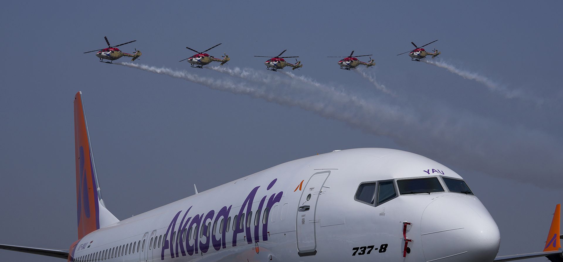 El avión 737-8 de Akasa Air se ve en primer plano mientras los helicópteros Sarang de la Fuerza Aérea de la India realizan una exhibición acrobática durante el El avión 737-8 de Akasa Air se ve en primer plano mientras los helicópteros Sarang de la Fuerza Aérea de la India realizan una exhibición acrobática durante el