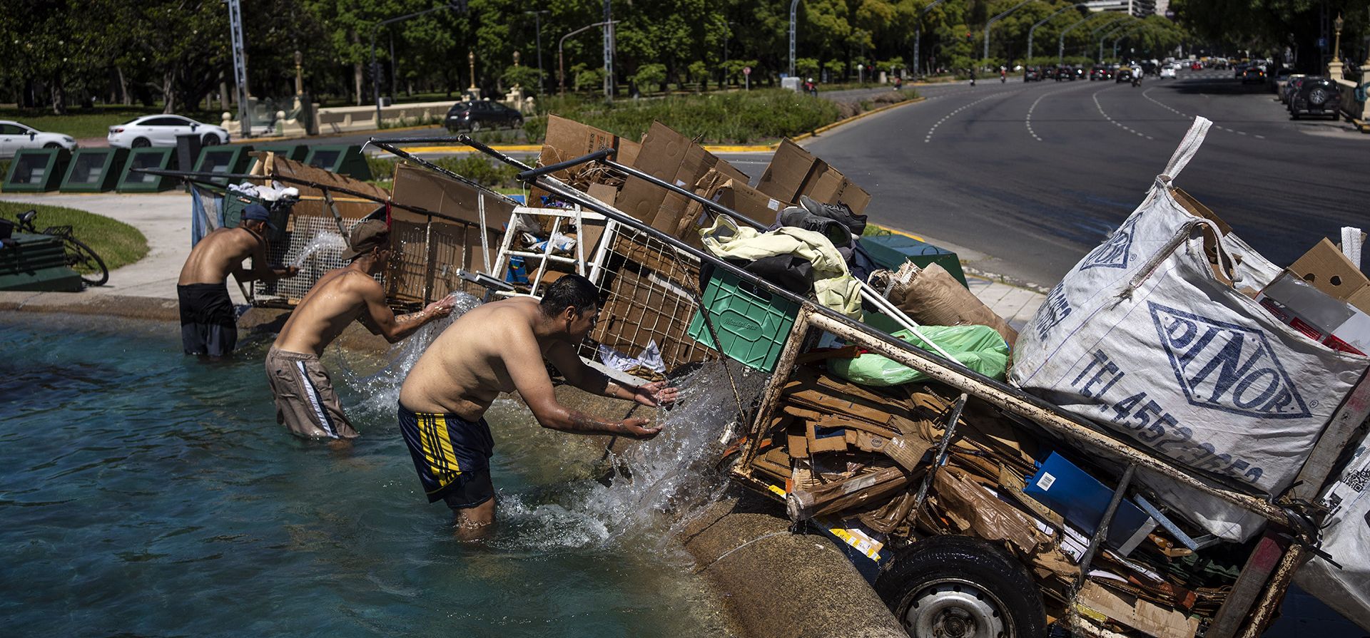 "Cartoneros" remojan sus desechos de cartón con agua antes de llevarlos a pesarlos en un centro de reciclaje, mientras se refrescan en una fuente en Buenos Aires, Argentina, el lunes 11 de diciembre de 2023. (Foto AP/Rodrigo Abd)