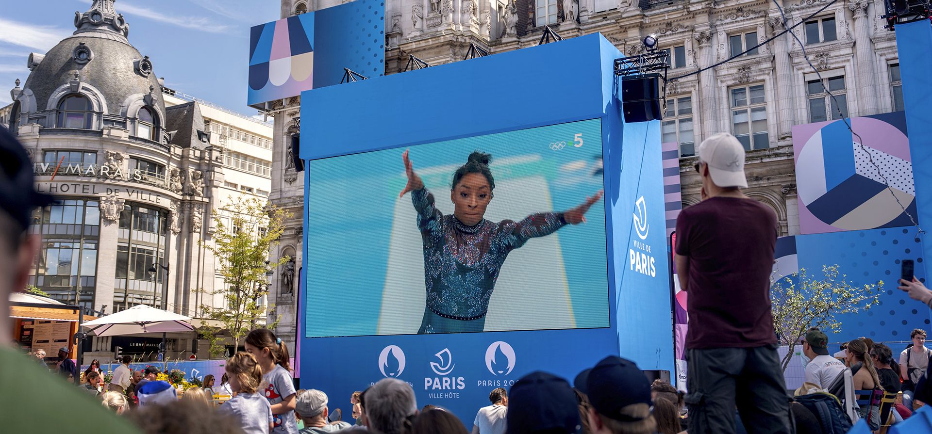 Los espectadores observan desde una zona para aficionados instalada en el Hotel de Ville, el ayuntamiento, mientras Simone Biles, de los Estados Unidos, realiza una prueba de salto de potro durante una ronda de clasificación de gimnasia artística femenina en los Juegos Olímpicos de Verano de 2024, el domingo 28 de julio de 2024, en París. (Foto AP/David Goldman) Los espectadores observan desde una zona para aficionados instalada en el Hotel de Ville, el ayuntamiento, mientras Simone Biles, de los Estados Unidos, realiza una prueba de salto de potro durante una ronda de clasificación de gimnasia artística femenina en los Juegos Olímpicos de Verano de 2024, el domingo 28 de julio de 2024, en París. (Foto AP/David Goldman)