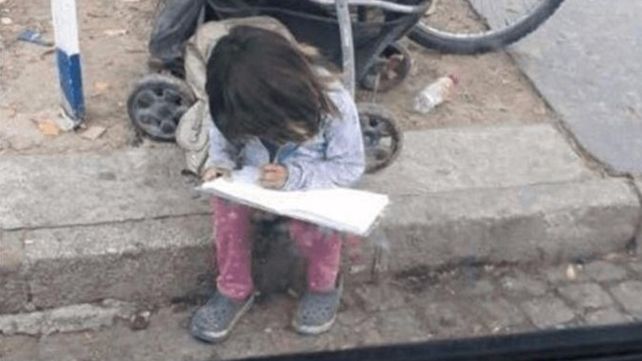 Una nena pide limosna mientras hace los deberes en la calle