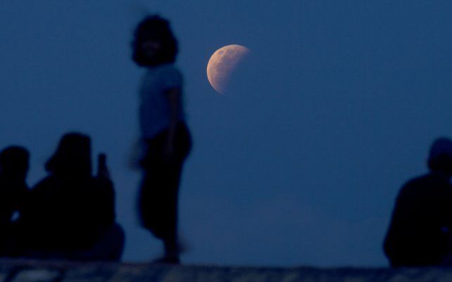 Los residentes ven el eclipse lunar en la playa de Sanur en Bali, Indonesia. El eclipse lunar total, también conocido como superluna de sangre, es el primero en dos años con el color naranja rojizo.