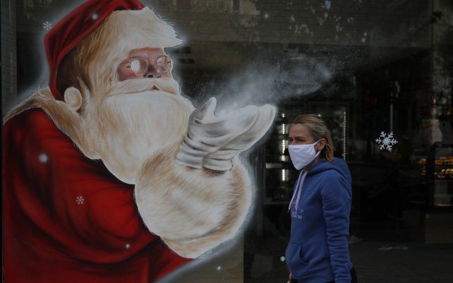 Una mujer pasa frente a un mural de Santa Claus del artista griego Solonas, que decora la vidriera de una panadería en Atenas. Grecia está preparada para extender sus medidas de cierre más allá del final de noviembre ante la propagación del COVID-19 y la presión sobre los hospitales, advirtió el ministro de Salud del país.