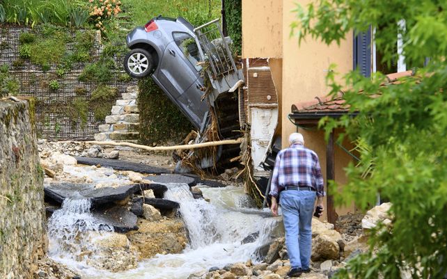 Una persona observa un vehículo incrustado en una casa después de una violenta tormenta en Cressier