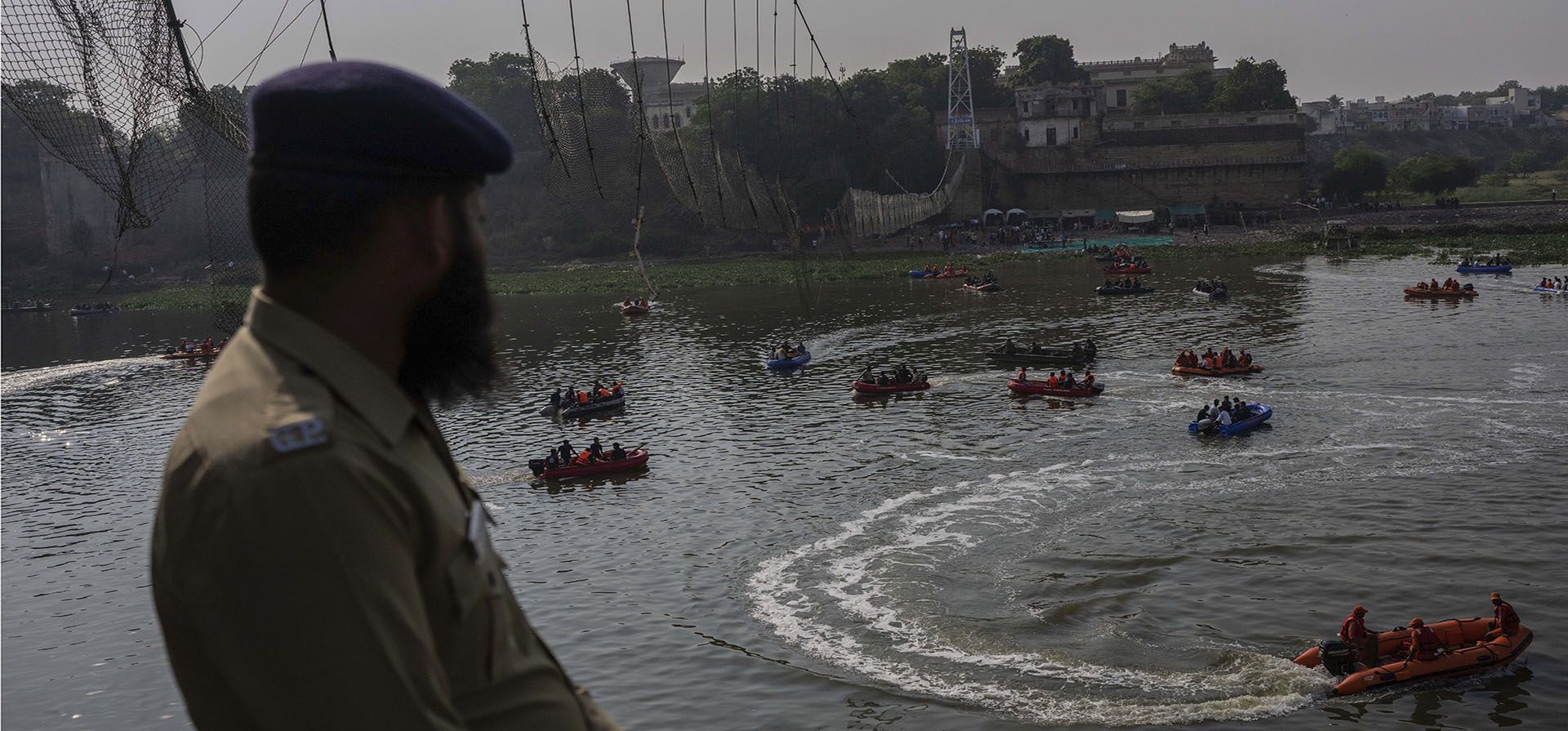 Un oficial de policía hace guardia mientras rescatistas en botes buscan en el río Machchu donde un puente peatonal se derrumbó el domingo en la ciudad de Morbi, en el estado occidental de Gujarat, India, el martes 1 de noviembre de 2022. Un puente colgante de cable de un siglo de antigüedad se derrumbó en el río el domingo a l a noche, enviando a cientos de personas a sumergirse en el agua en uno de los peores accidentes del país en años.