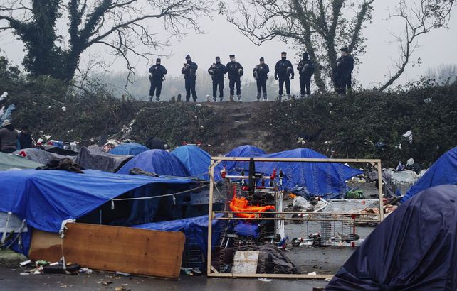 Fuerzas policiales observan el campamento improvisado para migrantes en Grande-Synthe, en el norte de Francia, el martes 16 de noviembre de 2021. La policía francesa estaba evacuando a los migrantes de un campamento improvisado cerca de Dunkerque, en el norte de Francia, donde al menos 1.500 personas se reunieron con la esperanza de lograrlo. a través del Canal de la Mancha hasta Gran Bretaña. 