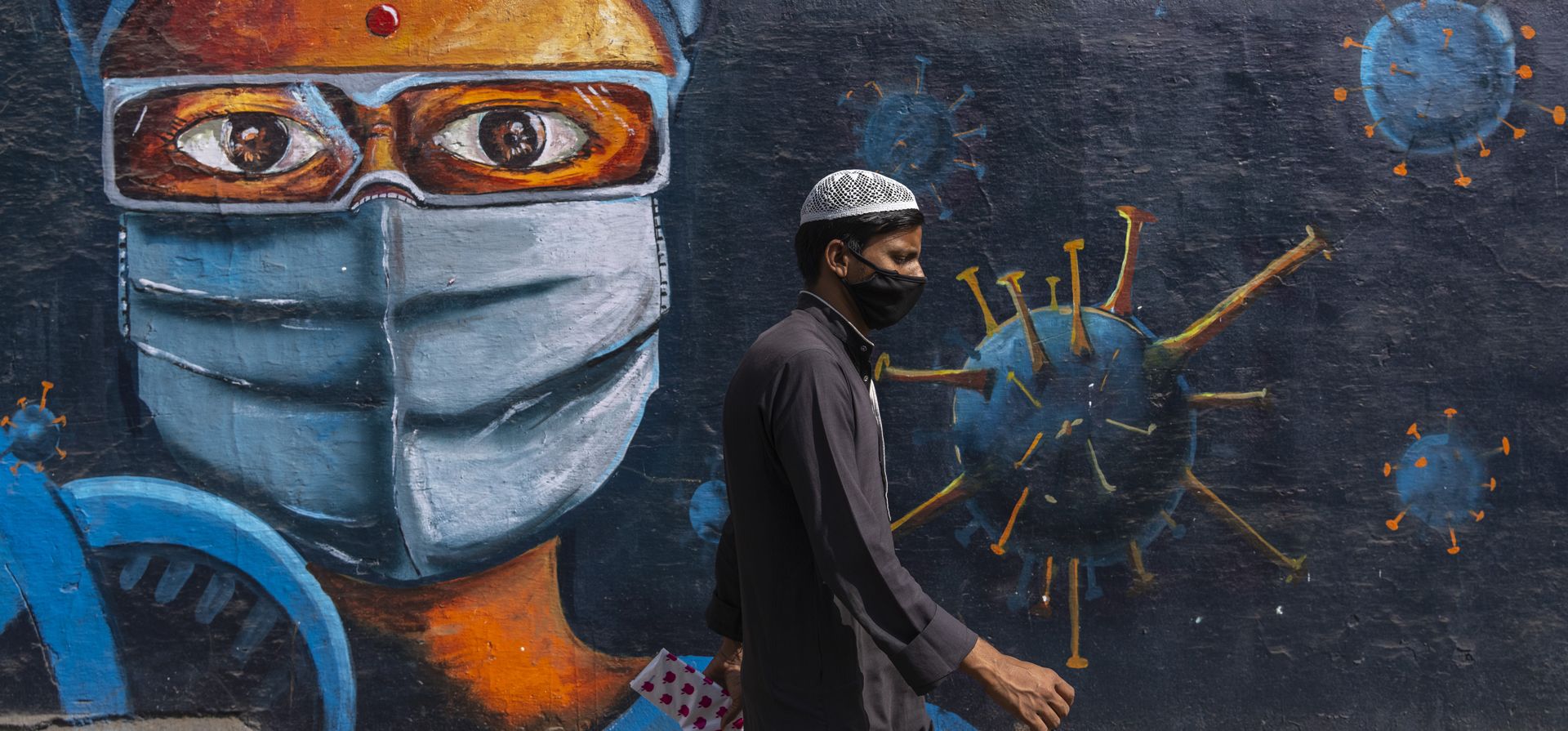 Un hombre pasa junto a un grafiti pintado en una pared para crear conciencia sobre la enfermedad del coronavirus, en Mumbai, India, el jueves 3 de febrero de 2022.