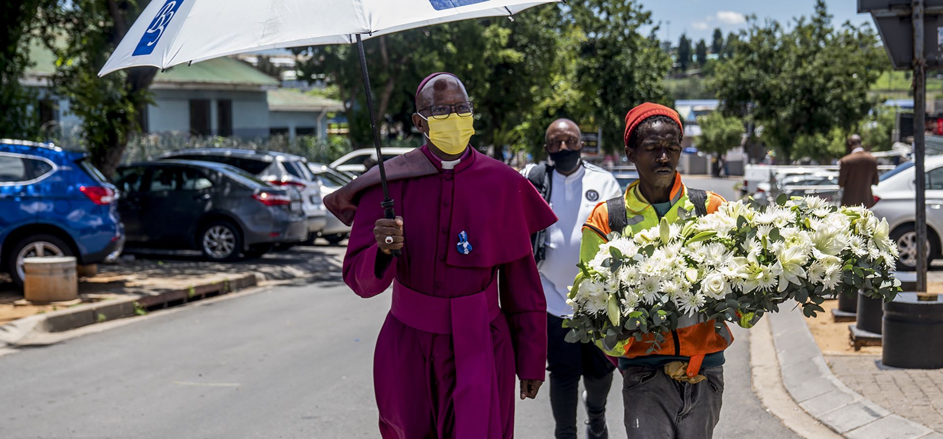 Un hombre con un ramo de flores en sus manos acompaña a un clérigo a un servicio conmemorativo para el arzobispo emérito anglicano Desmond Tutu frente a la casa Tutu en Soweto, el miércoles 29 de diciembre de 2021. El activista ganador del Premio Nobel de la Paz por la igualdad racial y los derechos LGBT murió el domingo a la edad de 90 años. Foto: AP