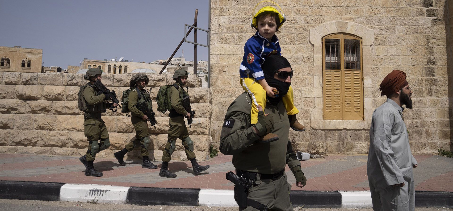 Un miembro de las fuerzas de seguridad israelíes lleva a un niño disfrazado de bombero en el desfile anual que marca la festividad judía de Purim en la parte controlada por Israel de la ciudad de Hebrón, en Cisjordania, el jueves 17 de marzo de 2022. El festival de Purim conmemora el rescate de judíos del genocidio en la antigua Persia.