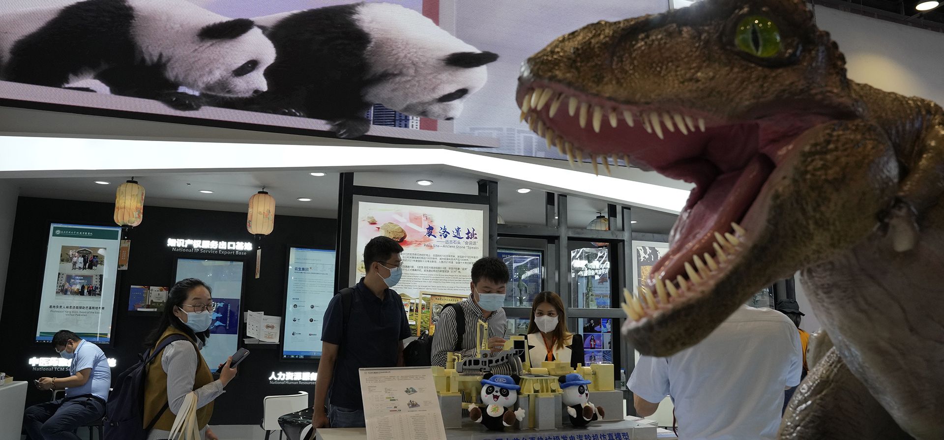 Un dinosaurio mecánico se muestra cerca de las imágenes del panda gigante en el stand de Sichuan durante la Feria Internacional de Comercio de Servicios de China (CIFTIS) en Beijing, el jueves 1 de septiembre de 2022.