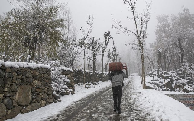 Un aldeano de Cachemira lleva un cilindro de gas para cocinar mientras camina por una carretera cubierta de nieve durante la primera nevada de la temporada en las afueras de Srinagar