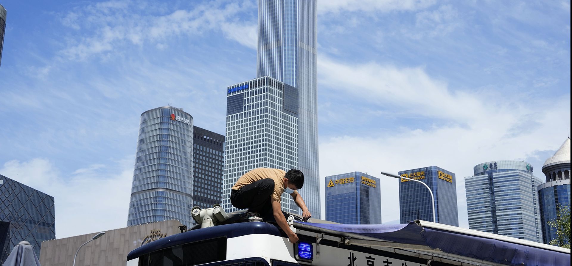 Un trabajador realiza mantenimiento en una cubierta de lona sobre un techo de una tienda, cerca del horizonte del Distrito Central de Negocios en Beijing, el jueves 28 de julio de 2022.