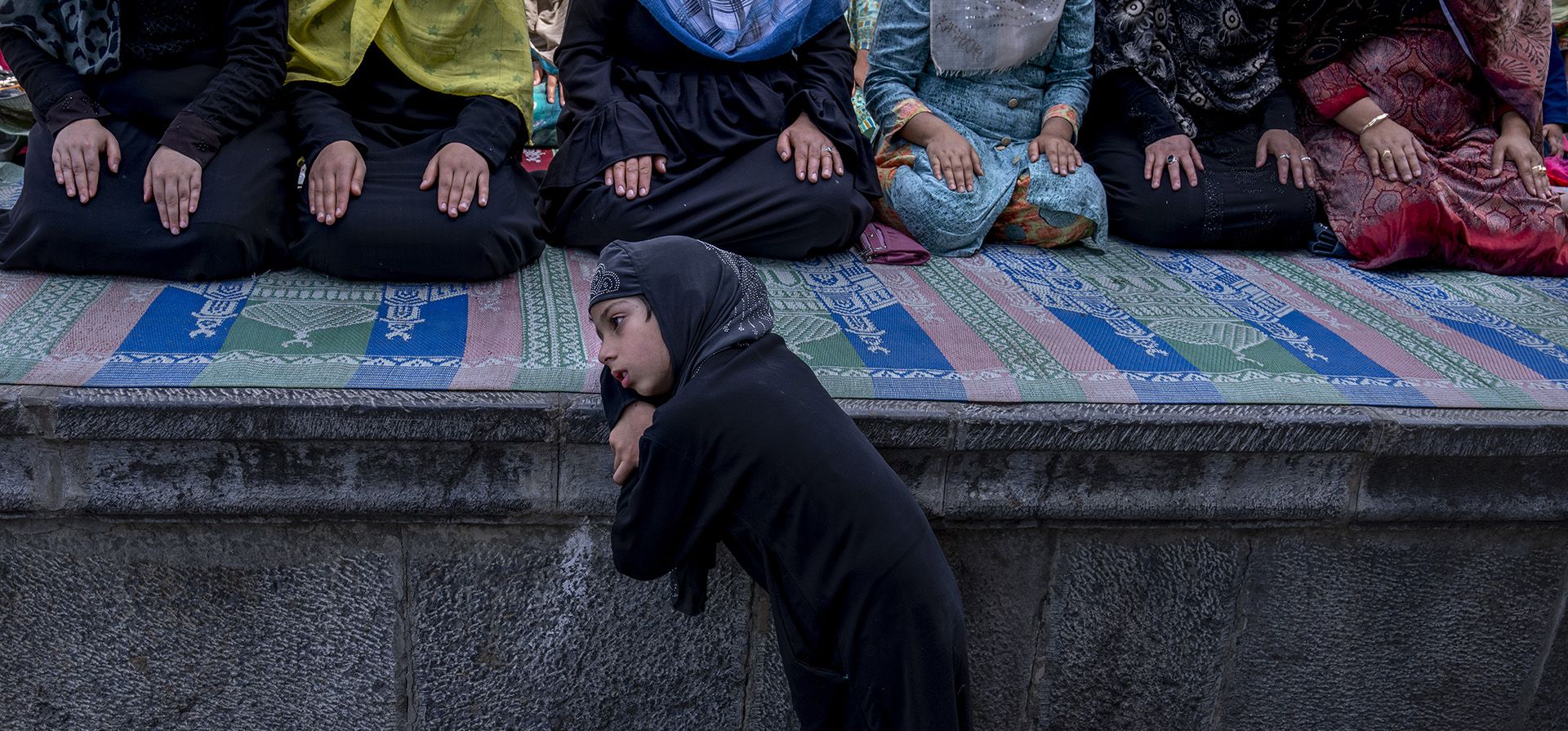 Una joven cachemira observa a sus familiares rezar fuera de la mezquita Shah-e-Hamdan, una de las mezquitas más antiguas de Cachemira, en Jumat-ul-Vida, el último viernes de Ramadán, en Srinagar, Cachemira india, el viernes 29 de abril de 2022.