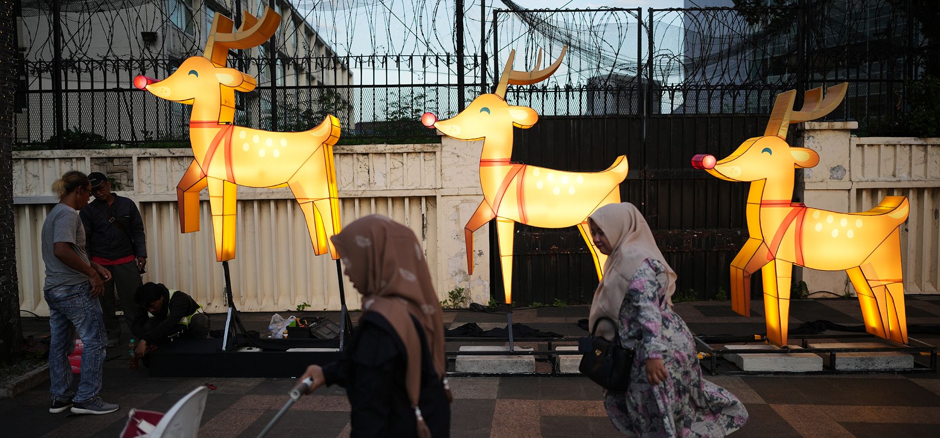 La gente pasa mientras los trabajadores instalan una exhibición de luces navideñas en Yakarta, Indonesia, el miércoles 24 de diciembre de 2025. (Foto AP/Dita Alangkara)