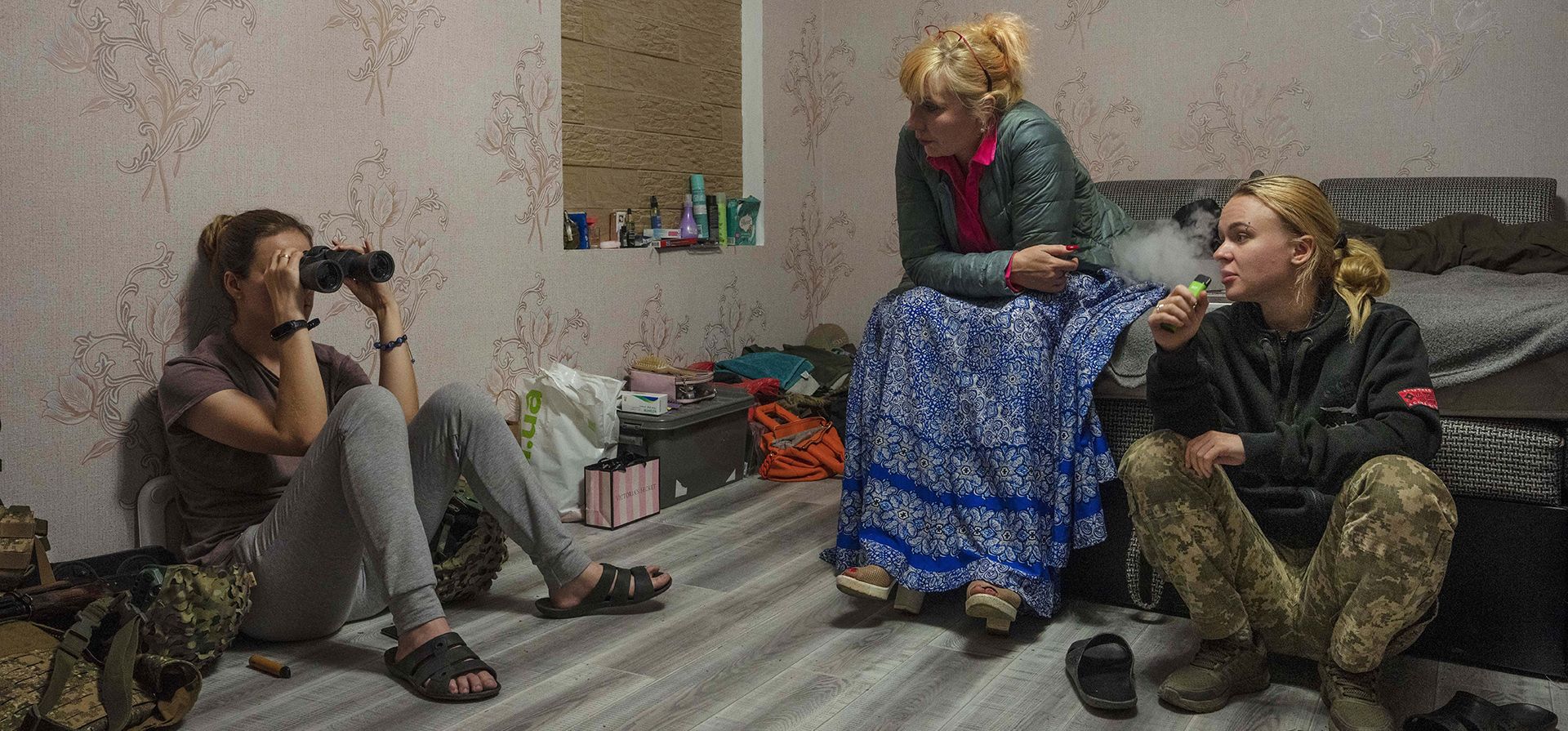 Una voluntaria médica, centro, entrega binoculares a una soldado mientras los prueba, y ayuda médica a un paramédico, a la derecha, en su base, en las afueras de Kurakhove, región de Donetsk, este de Ucrania, el jueves 21 de julio de 2022.