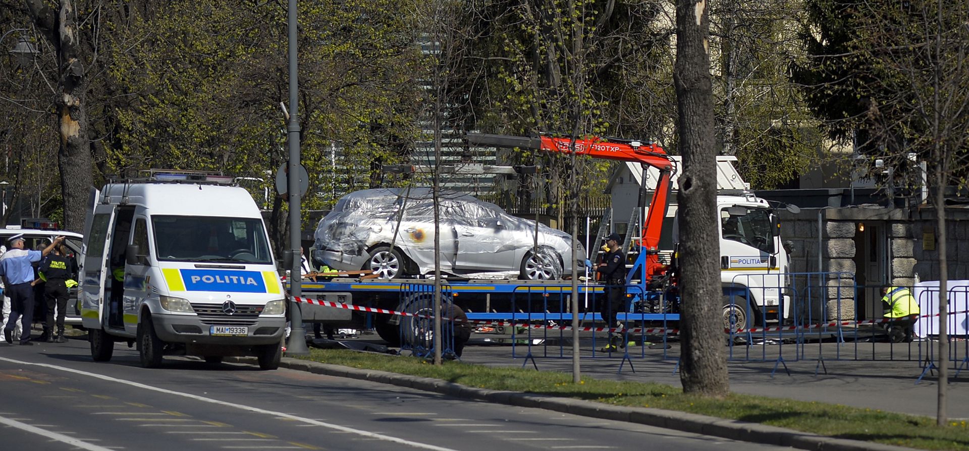 Un automóvil que se estrelló contra las puertas de la embajada rusa es elevado a una plancha de remolque en Bucarest, Rumania, el miércoles 6 de abril de 2022. La policía de la capital rumana dice que el automóvil se estrelló contra la puerta de la embajada rusa, estallando en llamas y muriendo al conductor.