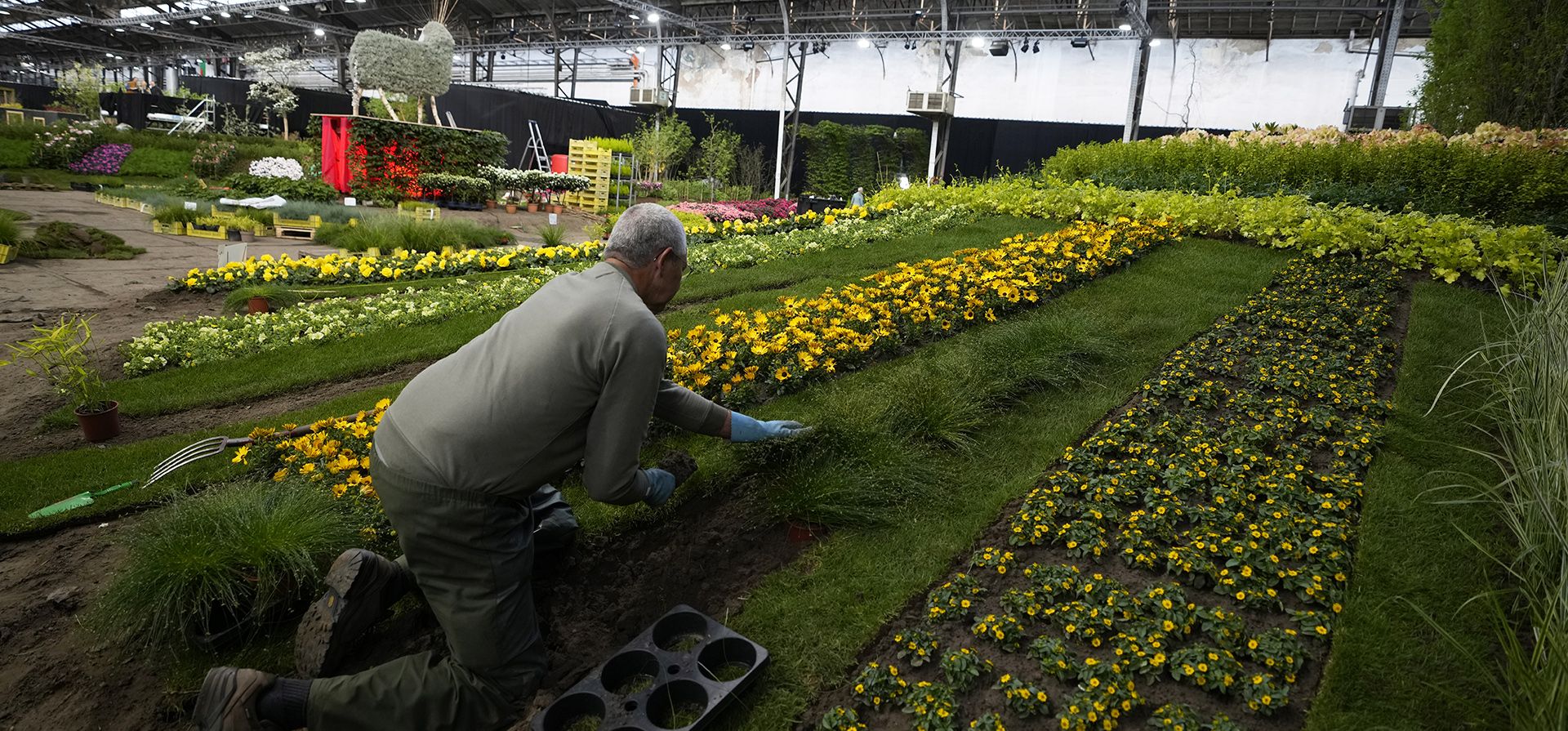 Un florista coloca hierbas entre hileras de flores mientras trabaja en una instalación en Ghent Floralies en Gante, Bélgica, el miércoles 27 de abril de 2022. Después de un aplazamiento de dos años debido a las regulaciones de COVID-19, la exhibición de flores ha regresado.