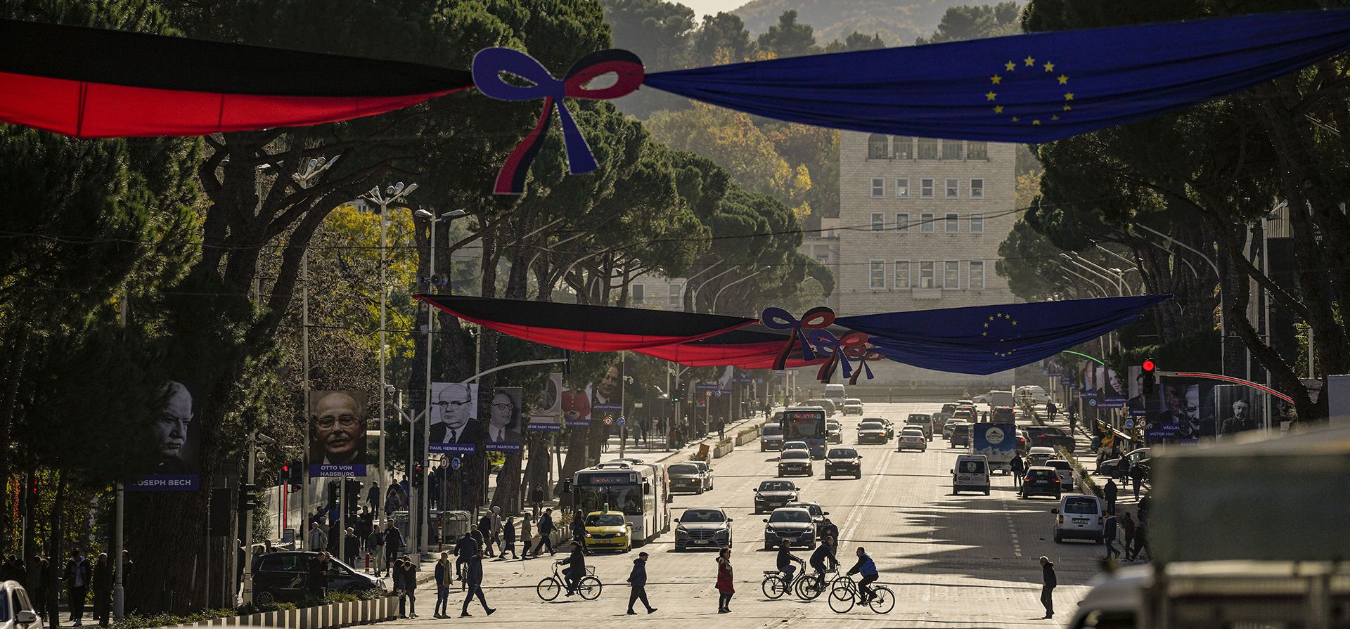 La gente cruza el bulevar Mártires de la Nación, decorado con banderas albanesas y de la UE, así como retratos de personalidades que contribuyeron al avance de la Unión Europea, en Tirana, Albania, el lunes 5 de diciembre de 2022. (Foto AP/Andreea Alexandru)
