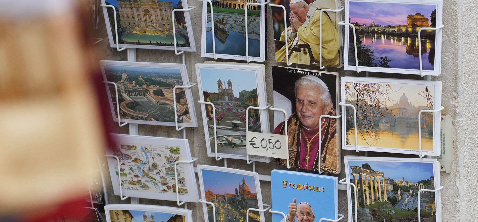 Postales del Papa Benedicto XVI, el Papa Francisco y el Papa Juan Pablo II se venden en un quiosco mientras el cuerpo del difunto Papa Emérito Benedicto XVI se exhibe en el interior de la Basílica de San Pedro en el Vaticano, el lunes 2 de enero de 2023. (Foto AP/Gregorio Borgia)