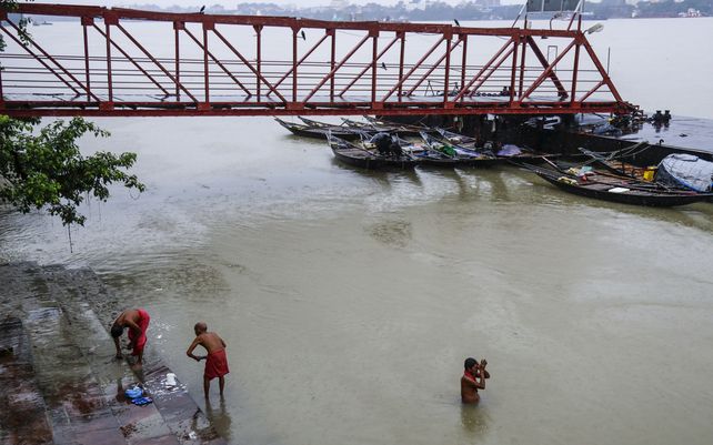 La gente se baña en el río Hooghly junto a un embarcadero vacío durante las lluvias monzónicas en Calcuta, India, el miércoles 29 de septiembre de 2021. La temporada de monzones de la India va de junio a septiembre.