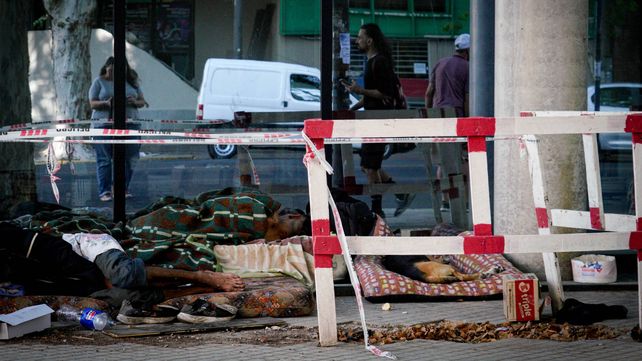 Los vidrios de un nuevo edificio en San Martín y Rueda reflejan a un grupo de personas durmiendo bajo la intemperie junto a su perro y rodeados por vallas provisorias de obras públicas