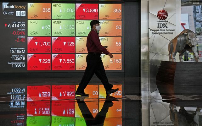 Un hombre pasa junto a un tablero electrónico que muestra los precios de las acciones en la Bolsa de Valores de Indonesia, en Yakarta, Indonesia. Las acciones globales cayeron ignorando un repunte en Wall Street liderado por compañías de tecnología y bancos.