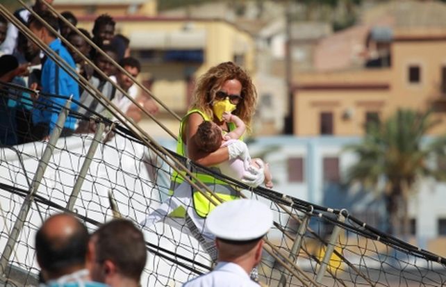 no me llames extranjero. Una inmigrante proveniente de España baja con su bebé en un puerto en Sicilia.
