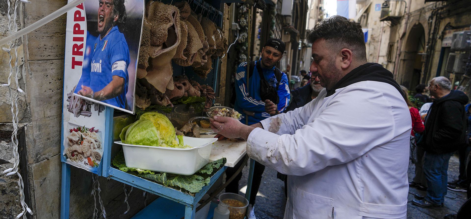 Una foto de Diego Armando Maradona se ve junto a un puesto de carnicería en el centro de Nápoles, Italia, el miércoles 19 de abril de 2023. Es una celebración que lleva más de 30 años, y los históricamente supersticiosos fanáticos de Napoli ya están pintando la ciudad de azul con anticipación del primer título de la liga italiana del equipo desde los días en que Diego Maradona jugaba para el club. (Foto AP/Andrew Medichini)