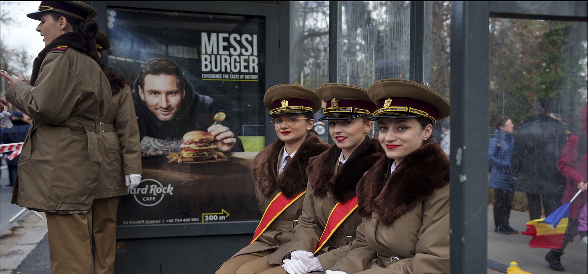 Cadetes militares sonríen mientras están sentados en una parada de autobús frente a un cartel que muestra a la estrella del fútbol argentino Lionel Messi antes de participar en el desfile del Día Nacional en Bucarest, Rumania, el viernes 1 de diciembre de 2023. (Foto AP/Vadim Ghirda)