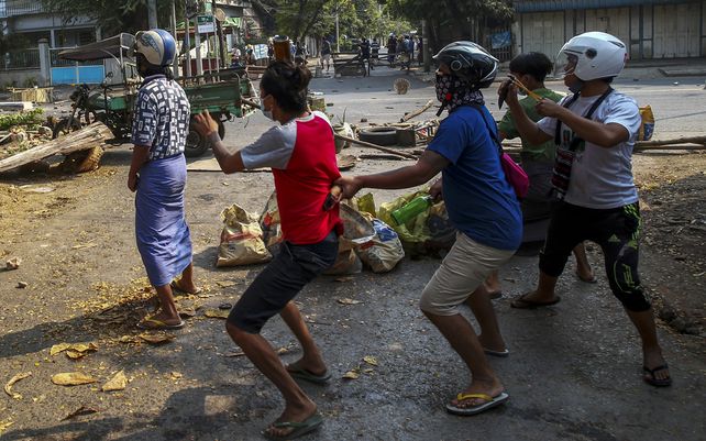 Manifestantes antigolpistas armados con hondas y una botella de vidrio reaccionan a la carga de policías antidisturbios en Mandalay