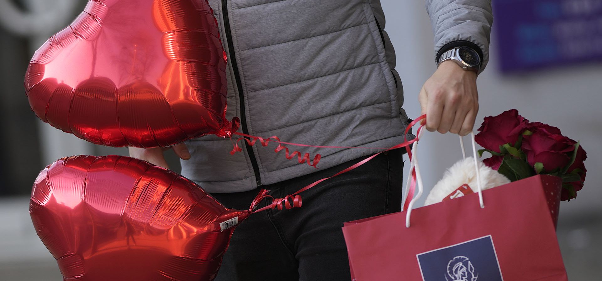 Un hombre lleva una bolsa con flores y chocolates mientras sostiene dos globos rojos en el Día de San Valentín en Londres, el martes 14 de febrero de 2023. (Foto AP/Alastair Grant)