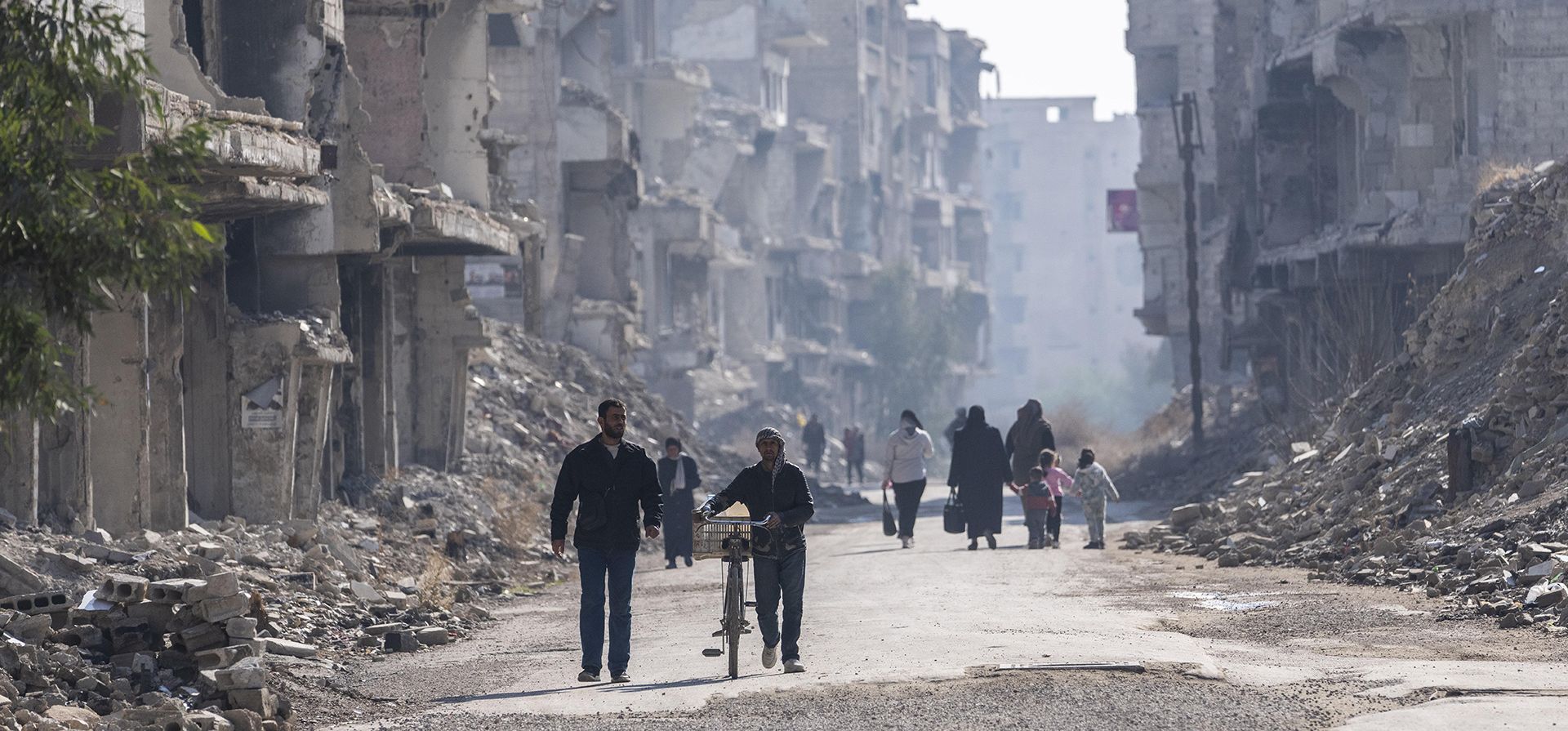 La gente camina cerca de edificios que fueron destruidos durante la guerra entre las fuerzas de oposición y el régimen de Assad, en el campo de refugiados palestinos de Yarmouk en Damasco, Siria, el jueves 2 de enero de 2025. (Foto AP/Mosa'ab Elshamy)