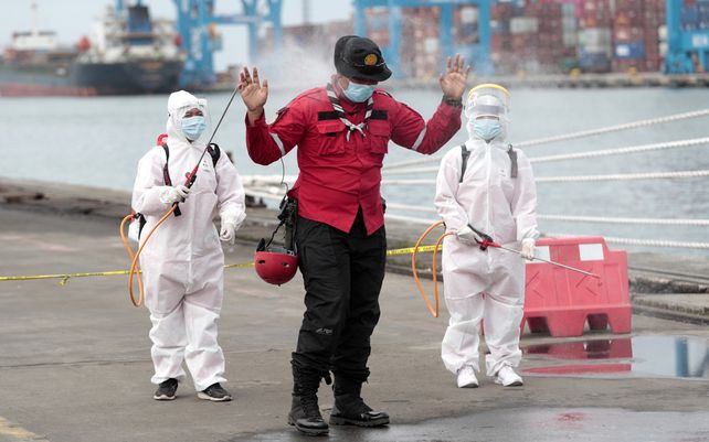 Miembros de la Cruz Roja Indonesia rocían a un socorrista con desinfectante después de clasificar partes de aviones y escombros recuperados del mar de Java