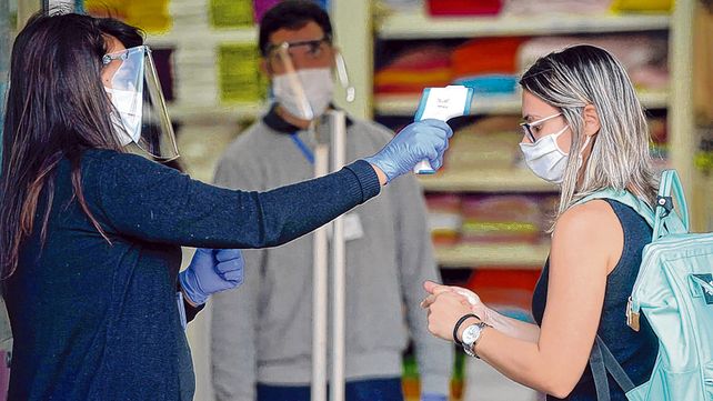 Nueva normalidad. Empleada de un comercio c&eacute;ntrico controla la temperatura corporal de una clienta previo a su ingreso al local.