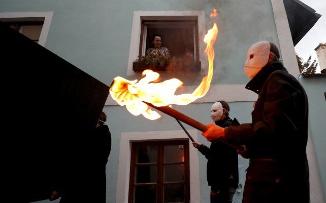 La gente observa desde la ventana de su casa a los participantes vestidos de negro, con máscaras, que participan en una procesión de Pascua por las calles de Ceske Budejovice, República Checa.