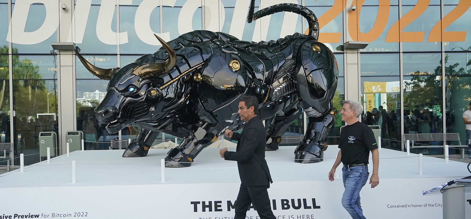 El alcalde de Miami, Francis Suarez, centro, y John Bartleman, presidente y director ejecutivo de TradeStation Group, caminan hacia el Miami Bull, el miércoles 6 de abril de 2022, en el Miami Beach Convention Center en Miami Beach, Florida. La estatua con forma de robot de un toro está destinado a emular el "Toro de carga" de Wall Street y se presentó para dar inicio a la conferencia Bitcoin 2022.