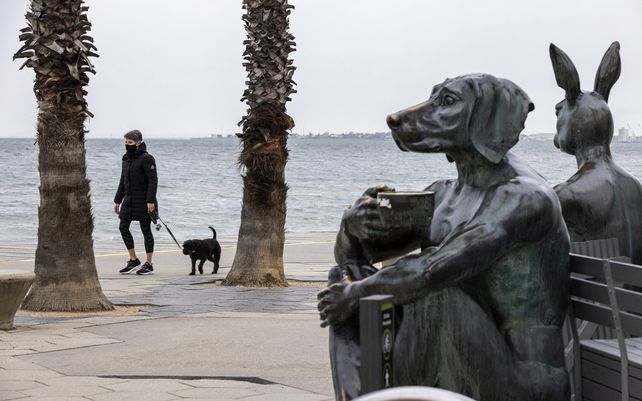 Una mujer pasea a un perro a lo largo de la playa de St. Kilda en Melbourne. La ciudad reportó 22 nuevos contagios