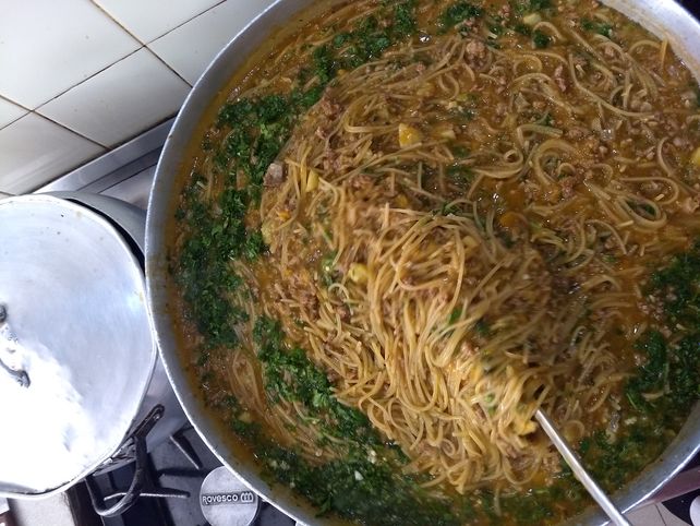 Manos que ayudan y cocinan tallarines con carne y verduras