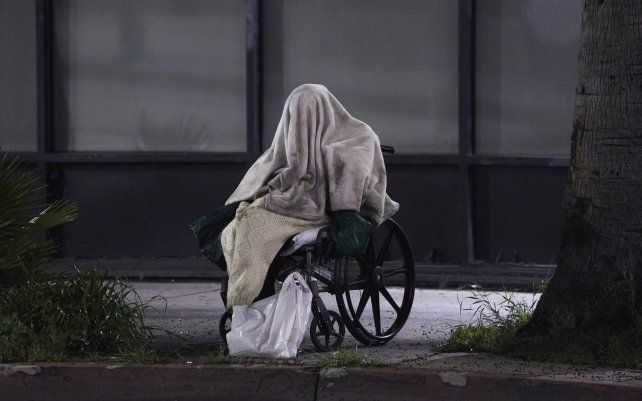 Una persona sin hogar sentada en una silla de ruedas bajo un clima lluvioso en Sunset Blvd., en el vecindario Echo Park de Los Ángeles.