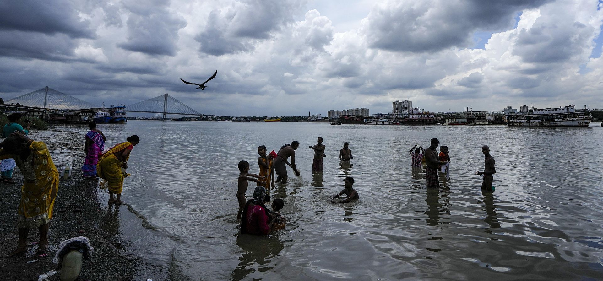 La gente se baña en el río Hooghly mientras las nubes monzónicas se ciernen sobre Calcuta, India, el viernes 5 de agosto de 2022.