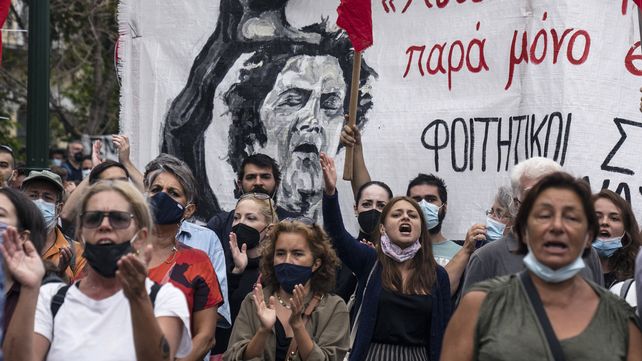 Una multitud aplaude y canta consignas frente a una pancarta que representa al difunto compositor griego Mikis Theodorakis mientras asisten a su ceremonia de despedida frente a la catedral de Atenas, el miércoles 8 de septiembre de 2021.