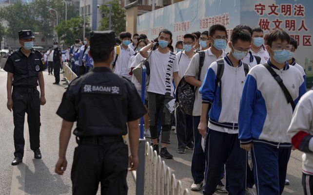 Guardias de seguridad controlan a los estudiantes con máscaras faciales para ayudar a frenar la propagación del coronavirus, al llegar a una escuela para el primer día de los exámenes nacionales de ingreso a la universidad de China, conocidos como gaokao, en Beijing.