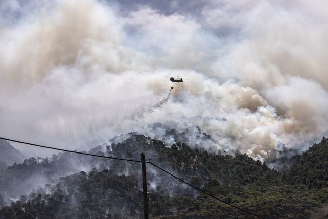 Un helicóptero militar arroja agua sobre un bosque cerca del pueblo de Schinos