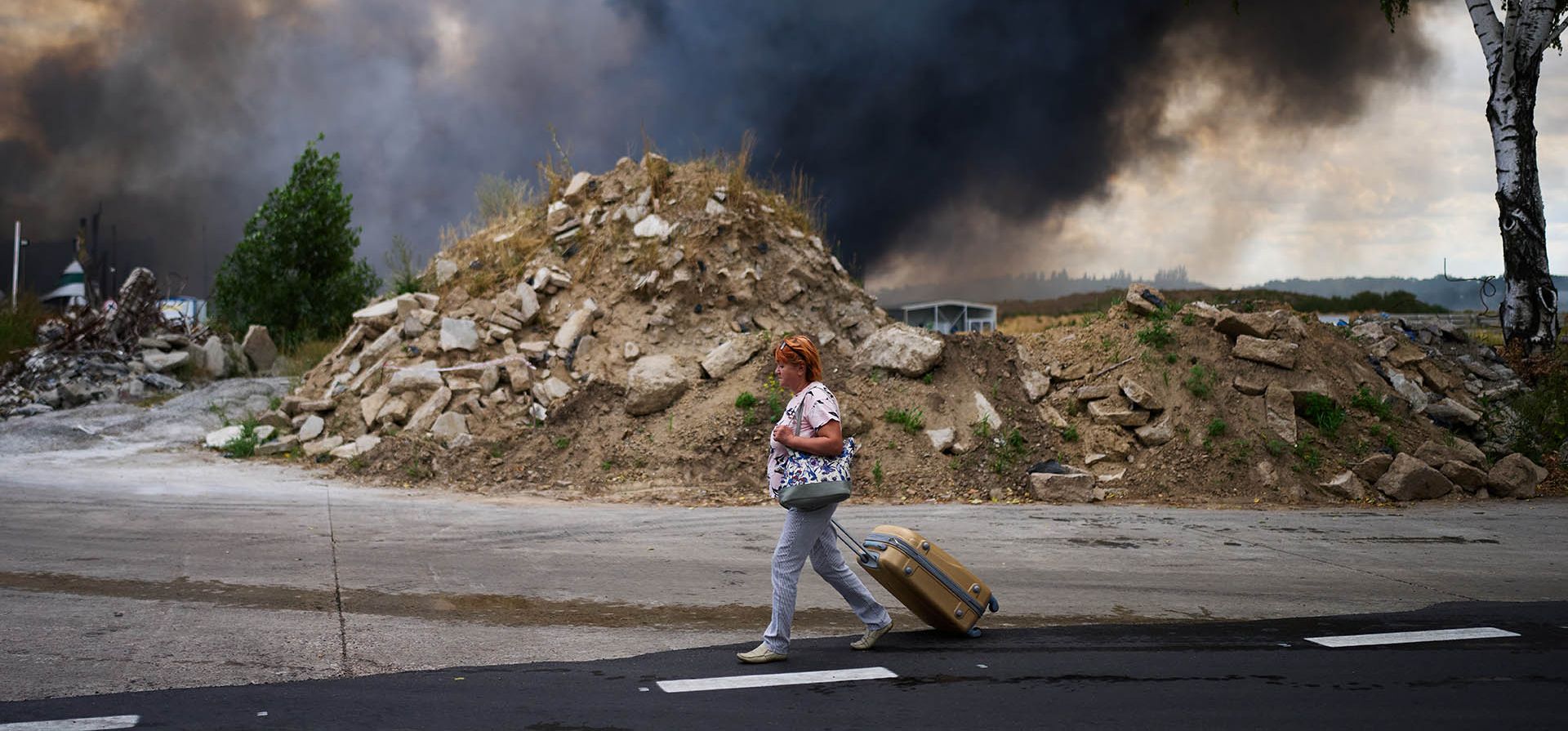 Una mujer camina por una carretera mientras sale humo de un almacén destruido tras un ataque con drones rusos en las afueras de Kiev, Ucrania, el jueves 27 de agosto de 2026. (Foto AP/Francisco Seco)